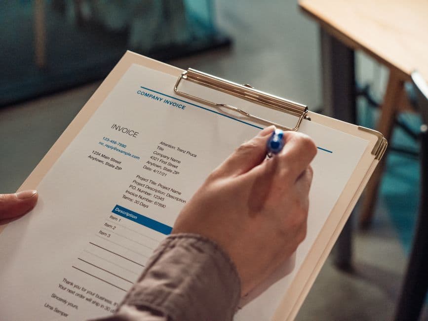 Hands signing a paper invoice on a clipboard