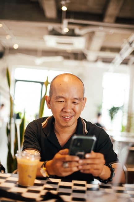 A man smiling at his phone in a cafe