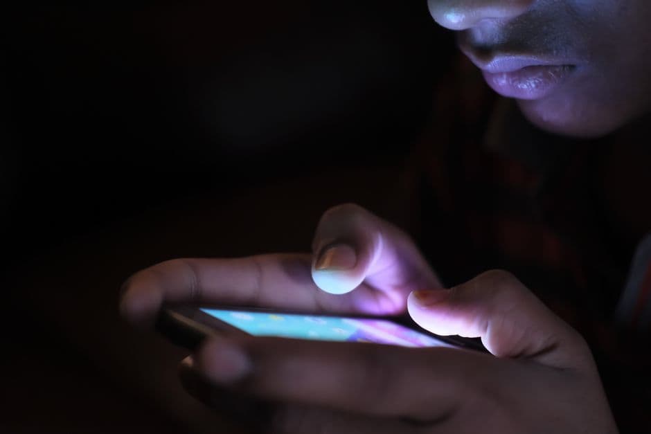 Hands holding a phone, its screen glowing in the dark