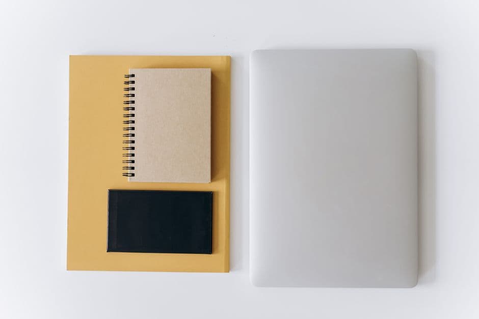A tidy desk seen from above: a closed laptop, a notebook, a phone