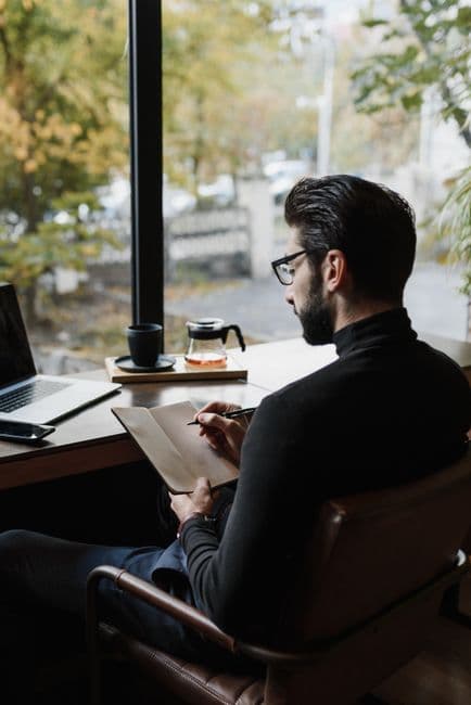 Someone writing in a notebook by a window